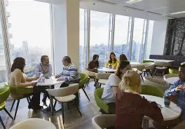 Multiple people meeting at different cafeteria styled tables talking over paperwork