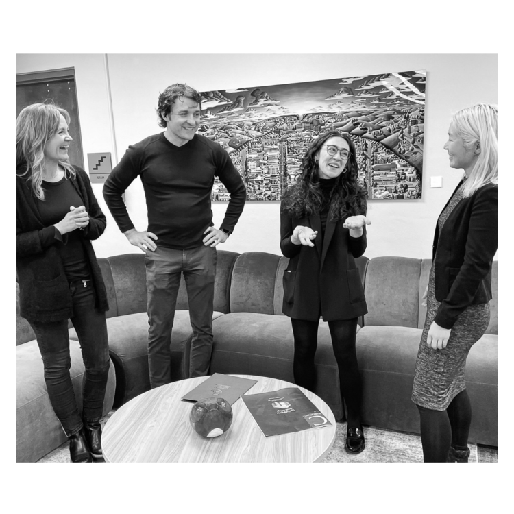 Three people engaged in conversation around a coffee table in a modern office setting.