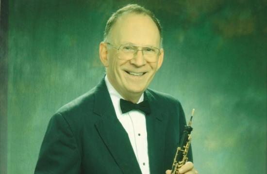 Donald John Schilling posing for a photo while holding an oboe.